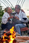 Senior couple hugging and drinking red wine by fire pit
