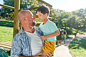 Father holding son with Down syndrome in sunny park