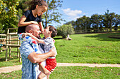 Father holding playful kids in sunny park