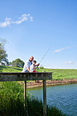 Father and son fishing on sunny lakeside dock