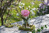 Rosenblüte (Rosa), Märzenbecher 'Gravetye Giant' und Traubenhyazinthen mit Zweigen in Vase und Nest aus Zweigen auf Gartentisch