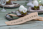 Easter egg with name on small nest with feathers and violet flowers, on plate with napkin and Easter greeting