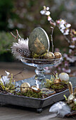 Etagere with golden Easter eggs and quail eggs, feathers and moss, Easter decoration