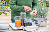 Woman dyeing Easter eggs, different colors in jars, wrapping egg with string