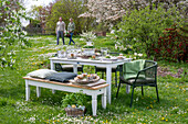Junges Paar vor gedecktem Tisch, Osterfrühstück mit Osternest und gefärbten Eiern in Eierbechern und Petersilie im Korb im Garten