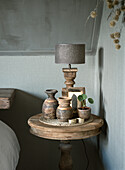 Round wooden table with antique vases, lamp and houseplant