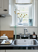 Kitchen with stainless steel sink, vintage taps and glass vase in front of window