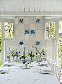 Dining table set with bouquets of flowers in front of a tiled wall with blue floral motifs