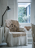 Reading chair with white cover and linen upholstery next to window with floor lamp