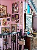 Staircase with flower paintings and vintage wooden chest of drawers in front of a pink wall