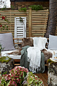 Sitting area with cushions, animal fur and textiles on the patio, wooden slatted privacy screen in the background