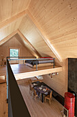 Loft with light-coloured wood panelling, gallery sleeping area, dining table below and red wood-burning stove