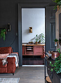 Living room with rust-brown velvet sofa and view of antique red chest of drawers in the hallway