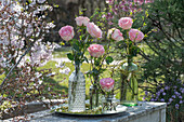 Langstielige rosa Rosen (Rosa) in verschiedenen Vasen auf Terrassentisch