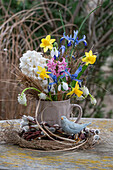 Spring bouquet of hyacinths, dwarf iris 'Clairette', snowdrops, grape hyacinths 'White Magic' in coffee cup, pussy willow and bird figurine on straw nest