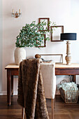 Wooden table with eucalyptus bouquet and black table lamp in front of white wall with picture frame