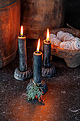 Three black stick candles with a fir branch on a dark stone table