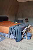 Bedroom with sloping ceiling, light-coloured wooden floor and rustic wooden stool