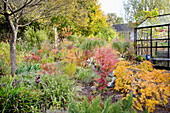 Bunter Herbstgarten mit hübsch dekoriertem Glasgewächshaus