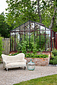 Garden with greenhouse and stone sofa in front of raised brick bed