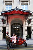 France,Paris,Royal Monceau hotel,woman riding in a retro side car in front of the hotel facade guarded by two valet