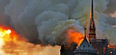 [ Unpublished - Exclusive ] France,Paris,area listed as World Heritage by UNESCO,Notre Dame Cathedral of 14th century Gothic architecture during the fire of 15th April 2019,incandescent frame of the transept spire and the nave,sunset in thick smoke
