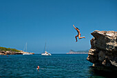 Spanien,Mädchen springt von kleiner Klippe am Strand La Basse,Ibiza