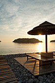 Griechenland,Sonnenschirm und Liegestühle am Strand gegenüber der Insel Spinalonga in der Morgendämmerung,Kreta
