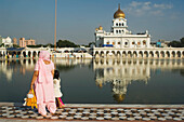Mutter und Kind im Gurudwara Bangla Sahib, einer Sikh-Anbetungsstätte in Delhi. Gurudwara Bangla Sahib ist der bekannteste Sikh-Gurdwara in Delhi. Der Tempel hat eine schöne goldene Kuppel und ein heiliges Wasserbecken, das als Saroyar bekannt ist. Der heilige Schrein