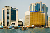 VAE,Bussling Wasserstraßenverkehr von Dubai Creek. Kleine Fähren, Fischerboote und private Schiffe überqueren die schmale Wasserstraße im Zentrum Dubais. Hohe Firmengebäude prägen die Skyline am Wasser, Dubai