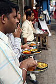 Locals eat plate-meal while standing up at this cheap on-street cafe in centre of Calcutta / Kolkata,the capital of West Bengal State,India,Asia.