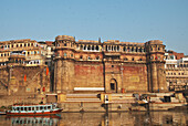 Indien, Uttar Pradesh, aufgenommen von einem Boot auf dem Ganges, Varanasi, Bonsale Ghat mit blauem und rotem Holzboot