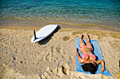Griechenland,Chalkidiki,Junge Frau beim Sonnenbaden am Strand mit Surfbrett im Sand,Ierissos