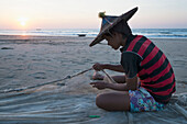 Myanmar (Burma),Irrawaddyi Division,Junger Mann befestigt Fischernetz am Strand bei Sonnenuntergang,Yea Thoe Dorf