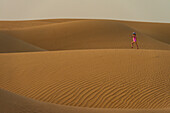 Girl In Pink Swimsuit Walking Across Sand Dunes At Dusk,Dubai,United Arab Emirates