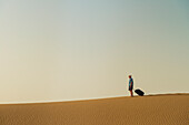Barefoot Man With Suitcase On Sand Dune,Dubai,United Arab Emirates