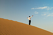 Mann in eleganter Kleidung winkt auf einer Sanddüne, Dubai, Vereinigte Arabische Emirate