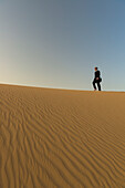 Mann im schicken Anzug, der in der Abenddämmerung auf einer Sanddüne spazieren geht, Dubai, Vereinigte Arabische Emirate