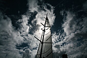 Silhouette eines Mannes, der auf einen Segelmast klettert, vor einem blauen, wolkenverhangenen Himmel mit Sonnenuntergang beim Mt Gay Rum Yacht Race, das die Insel Grenada umrundet,Grenada,Karibik