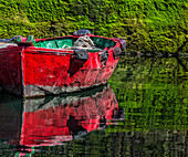 Small,wooden fishing boat moored to the shore with a mirror image reflection in the calm water in the coastal town of Getaria,Getaria,Gipuzkoa,Spain