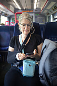 Ältere Frau fährt mit öffentlichen Verkehrsmitteln und benutzt ihr Smartphone