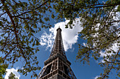 Niedriger Winkel des Eiffelturms vor einem blauen Himmel mit Wolken, umgeben von Ästen,Paris,Frankreich