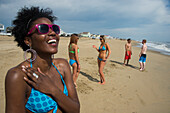 Gruppe von Freunden in Badekleidung am Virginia Beach, mit einer jungen Frau im Vordergrund, die lächelt und eine rosa gerahmte Sonnenbrille trägt, First Landing State Park, Virginia, USA, Virginia Beach, Virginia, Vereinigte Staaten von Amerika