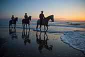Cowboys reiten bei Sonnenaufgang am Virginia Beach im First Landing State Park, Virginia, USA, Virginia Beach, Virginia, Vereinigte Staaten von Amerika