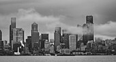 Seattle skyline form West Seattle across Elliott Bay on a rainy afternoon with wisps of low clouds and fog drifting through the tall buildings,Seattle,Washington,United States of America