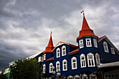 Gebäude mit dunkelblauer Fassade, weißen Fensterrahmen und roten Türmchen in der Hafenstadt Akureyri, Akureyri, Island