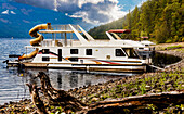 Ein Hausboot, das an einer Anlegestelle am Ufer des Shuswap Lake geparkt ist, Shuswap Lake, British Columbia, Kanada