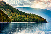 Ein Hausboot, das am Ufer des wunderschönen Shuswap Lake geparkt ist, mit Sonnenstrahlen, die eine dramatische Beleuchtung und Reflexionen über den Bergen und dem Wasser während der Herbstsaison erzeugen, Shuswap Lake, British Columbia, Kanada