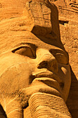 Close-up of one of the Ramses II statues carved out of the mountainside at the front of the Great Sun Temple of Abu Simbel with golden light,Abu Simbel,Nubia,Egypt