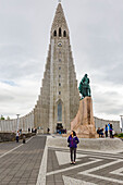 Eine Touristin posiert vor der ikonischen Hallgrimskirkja, der höchsten Kirche Islands, Reykjavik, Island